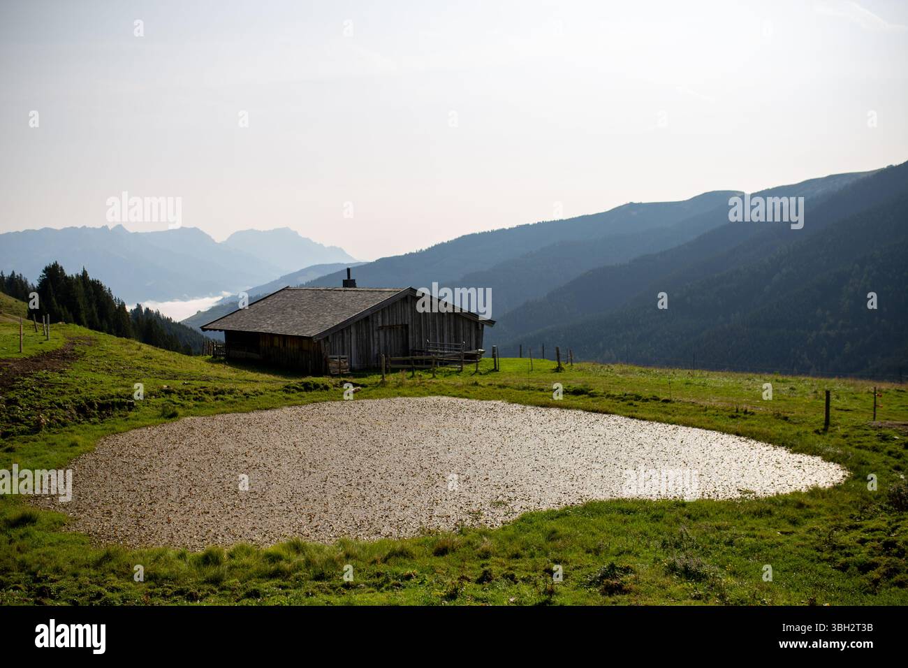 Eine traditionelle Holzhütte mit dunklem Dach steht auf einem grasbewachsenen Hang, begleitet von einem kleinen Teich oder künstlichem See Stockfoto