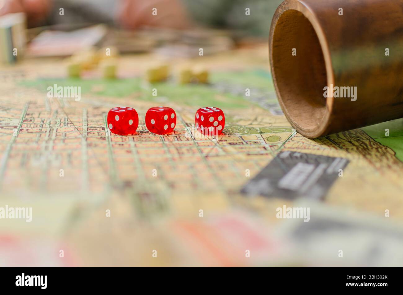 Nahaufnahme. Ein Makrofoto fängt den aufregenden Moment eines Tabletop-Brettspiels ein. Drei leuchtend rote Würfel stehen im Fokus und ruhen auf einer farbenfrohen Spielboa Stockfoto
