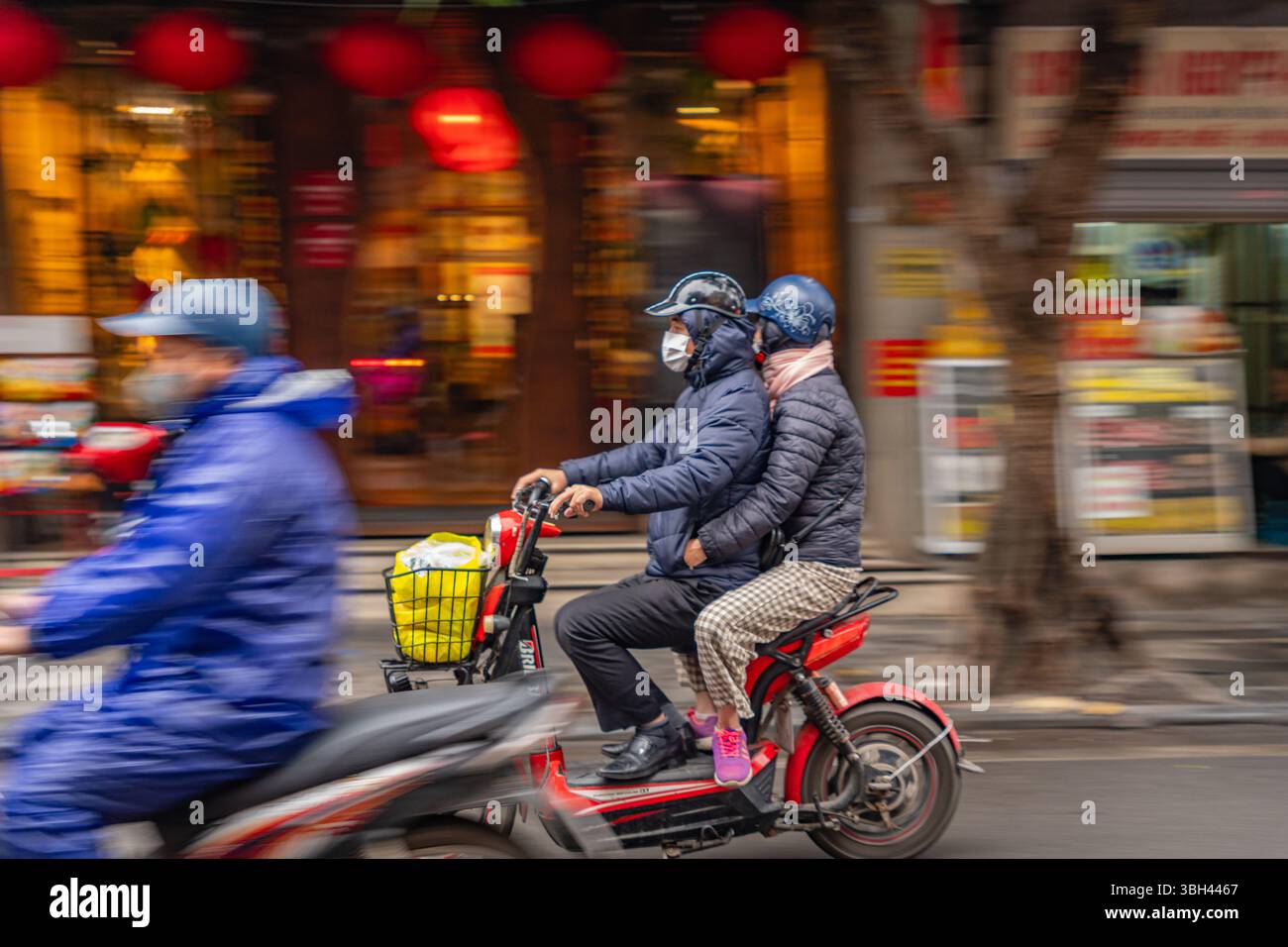 Hanoi, Vietnam, 6. Februar 2025: Motorroller, der sich schnell bewegt, während der Passagier auf der Straße durch die Stadt fährt, mit Bewegungsunschärfe im Hintergrund. Stockfoto