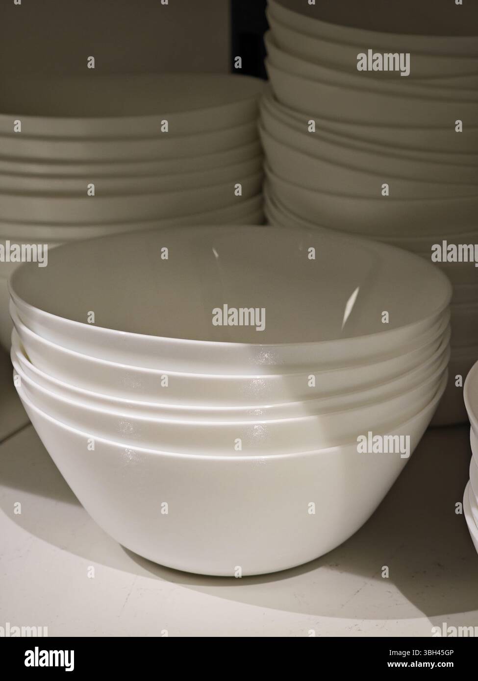 Ein hübsches Arrangement weißer Teller steht auf einem Küchenregal und besticht durch sein schlichtes Design und die perfekte Stapelbarkeit. Stockfoto