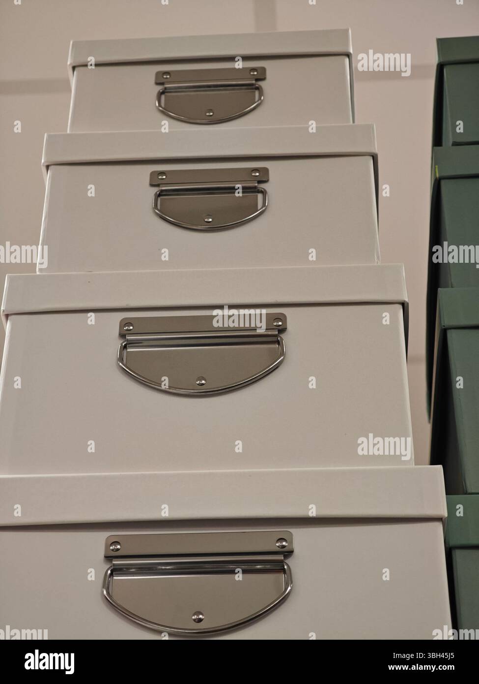 Vier Aufbewahrungsboxen sind vertikal angeordnet und verfügen über glatte, helle Oberflächen und glänzende Metallgriffe. Der Hintergrund zeigt einen an Stockfoto