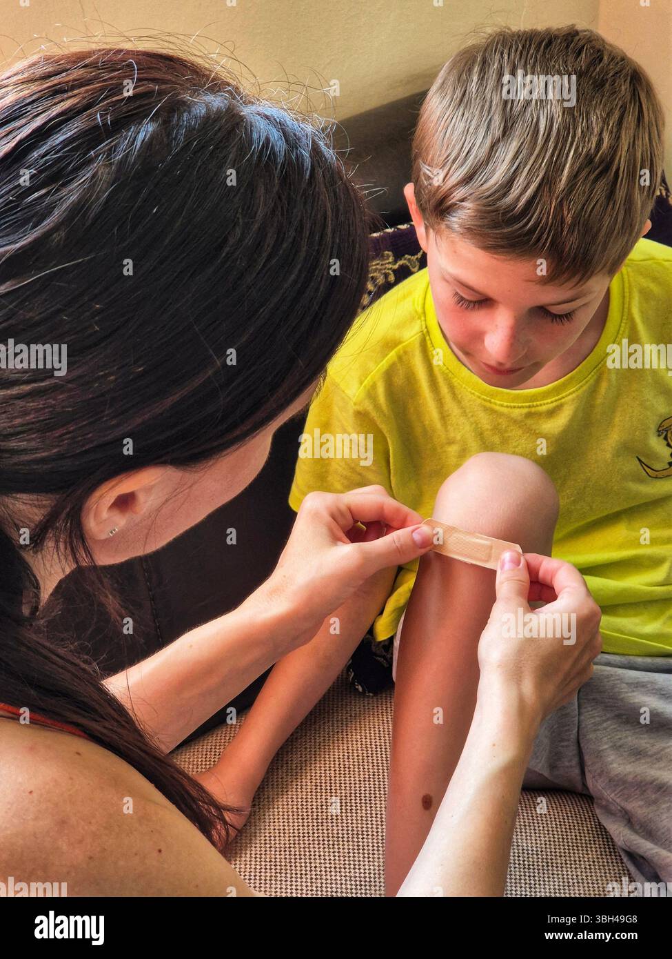 Mutter Frau legt medizinisches Pflaster auf das Knie des Kindes. Die Hand der Mutter mit Klebepflaster schützt das Bein des Kindes vor Wunden. - Smartphone-aufgenommenes Stockfoto