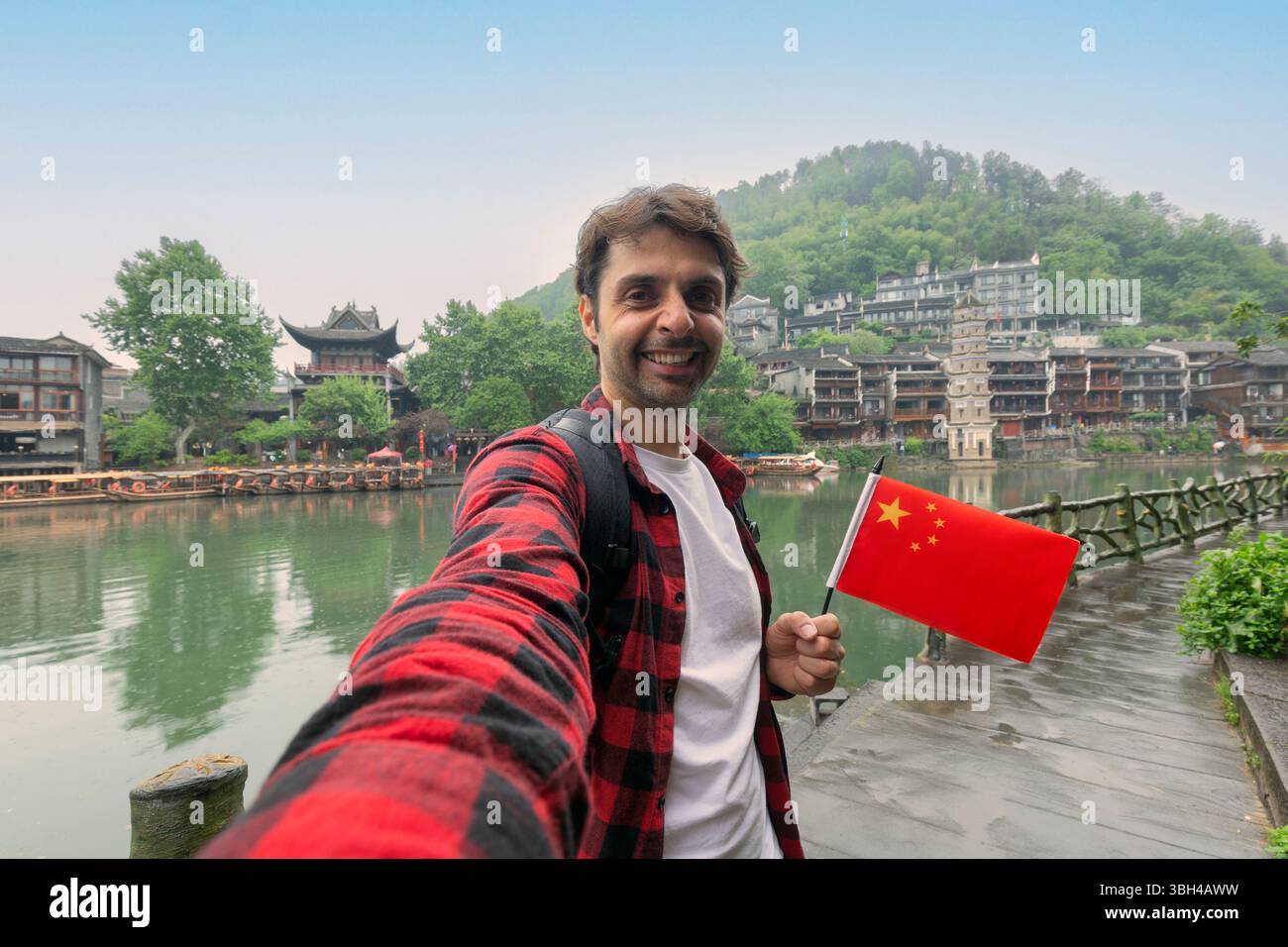 Urlaub in China genießen. Reisen und Technologie. Junger Mann mit chinesischer Flagge, der Selfie in Fenghuang macht Stockfoto