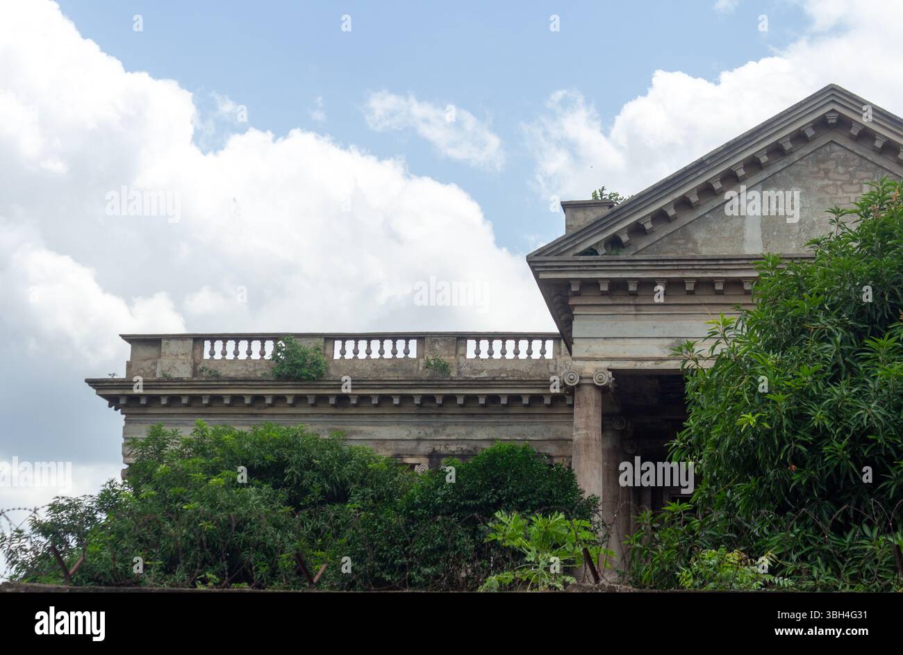 Neoklassizistisches Kolonialgebäude mit kunstvollem Giebel und üppigem Grün unter dem blauen Himmel – historische Architektur in tropischer Umgebung Stockfoto