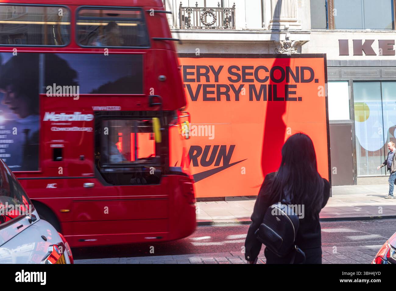 London, UK, 5. Mai 2025, Red Bus und Frau in schwarzem Mantel in Unschärfe und Nike Ad on A City Street. Stockfoto