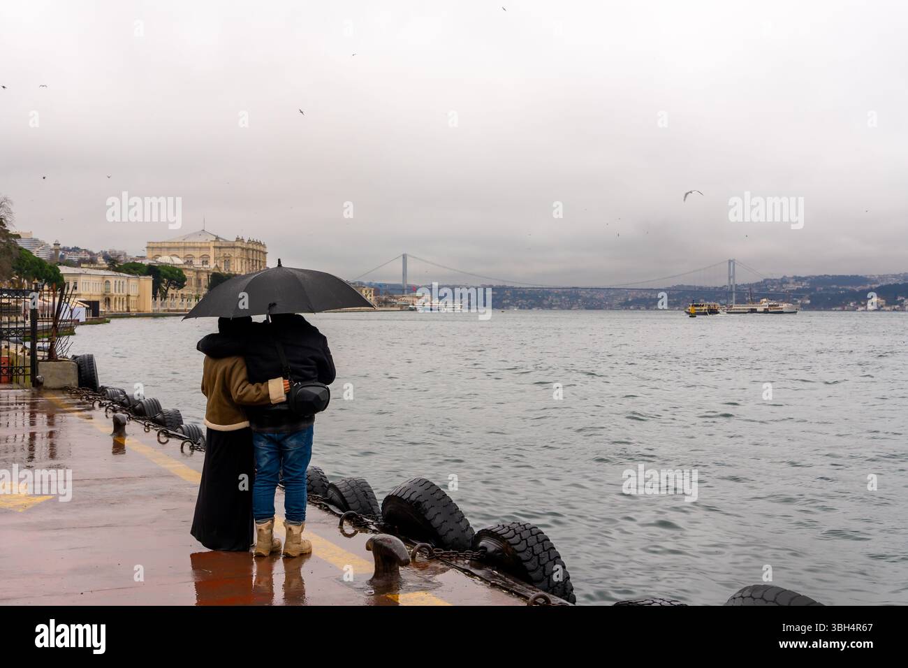 Ein junges Paar mit Regenschirmen in der Hand blickt bei regnerischem Wetter über die Bosporusbrücke. Reisen Stockfoto