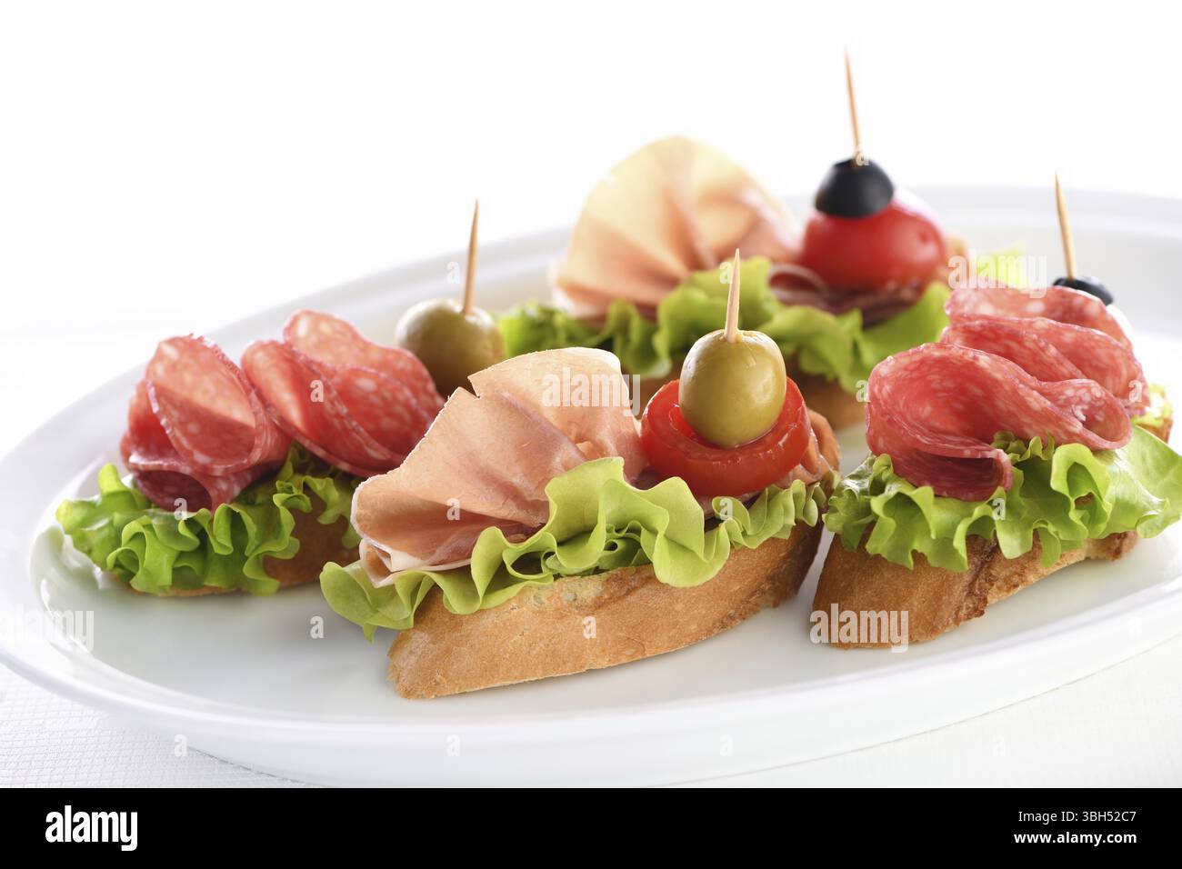 Zarte Baguette Canapes mit Blattsalat, Salami oder Parmaschinken, Tomaten, Mozzarella und Oliven. Delikatesse-Platte für die Party Stockfoto