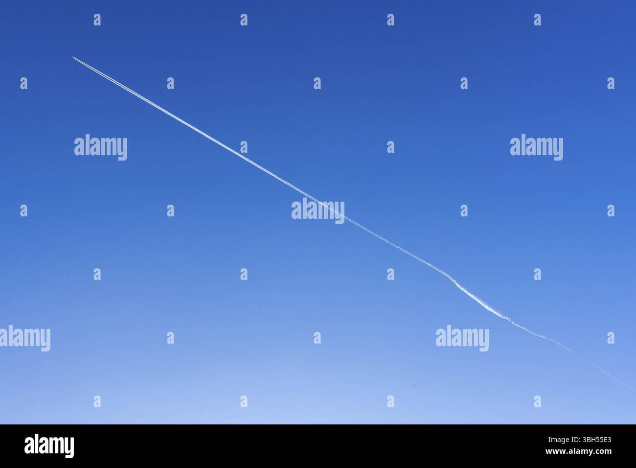 Das Flugzeug am blauen Himmel hinterlässt weiße Streifen hinter sich. Die Richtung ist diagonal. Sie kann als Hintergrund verwendet werden. Leerzeichen für Text Stockfoto