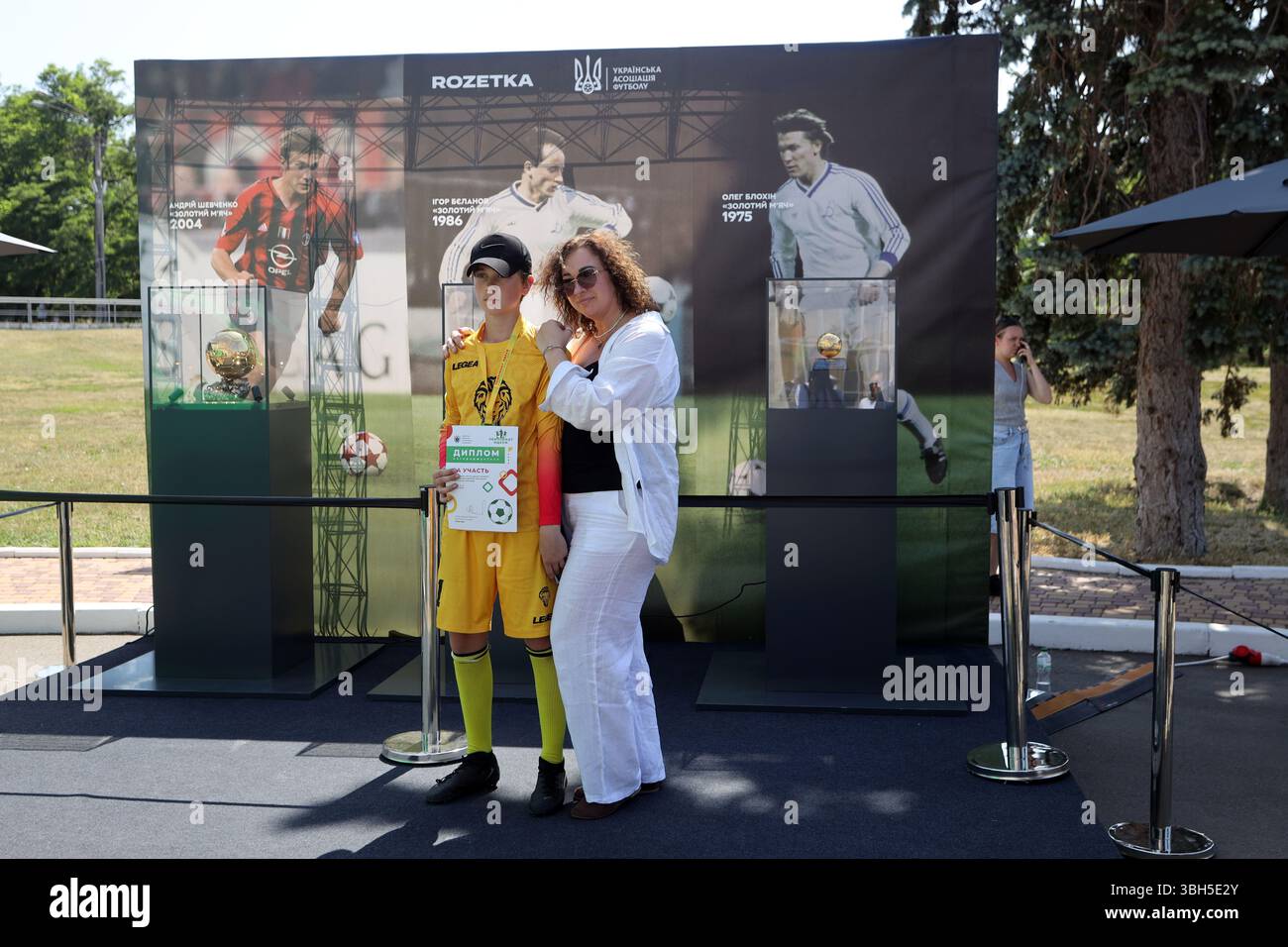 Der junge Fußballspieler und seine Mutter posieren für ein Foto vor den Golden Balls im zentralen Kultur- und Freizeitpark Taras Schevchenko. Der Zweck der Veranstaltung ist die Beschaffung von Geldmitteln durch den Kauf von Souvenirs für das Kinderturnier „Schulball“ des ukrainischen Fußballverbandes. Der Ballon d’Or („Goldener Ball“) ist ein jährlicher Fußballpreis, der seit 1956 von der französischen Zeitschrift France Football verliehen wird, um den Spieler zu ehren, der in der vergangenen Saison die besten Leistungen gezeigt hat. Drei ukrainische Spieler haben diese Auszeichnung erhalten: OLEH Blokhin 1975, Ihor Bielanov 1986 und Andrii Schewtschenko Stockfoto