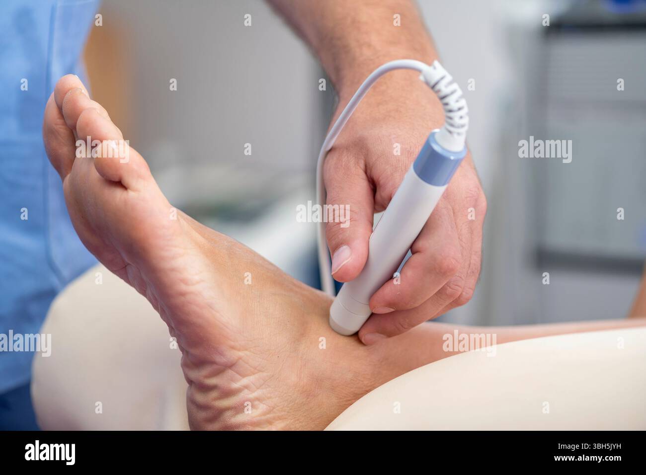 Der Physiotherapeut wendet eine Lasertherapie am Knöchel des Patienten an, um Entzündungen zu reduzieren und die Heilung zu fördern. Die fokussierte Lichtbehandlung zielt darauf ab, die Erholung von Verletzungen zu beschleunigen. Stockfoto