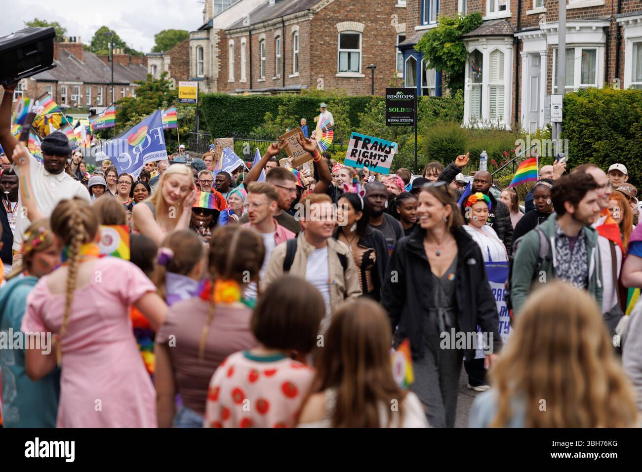 York, Großbritannien. 7. Juni 2025. Die Parade im York Pride 2025 führt durch das Stadtzentrum von York. Kinder beobachten, wie ein Mitglied der Parade das Schild „Trans Rights Now“ hochhält. Quelle: Katy Blackwood/Alamy Live News Stockfoto