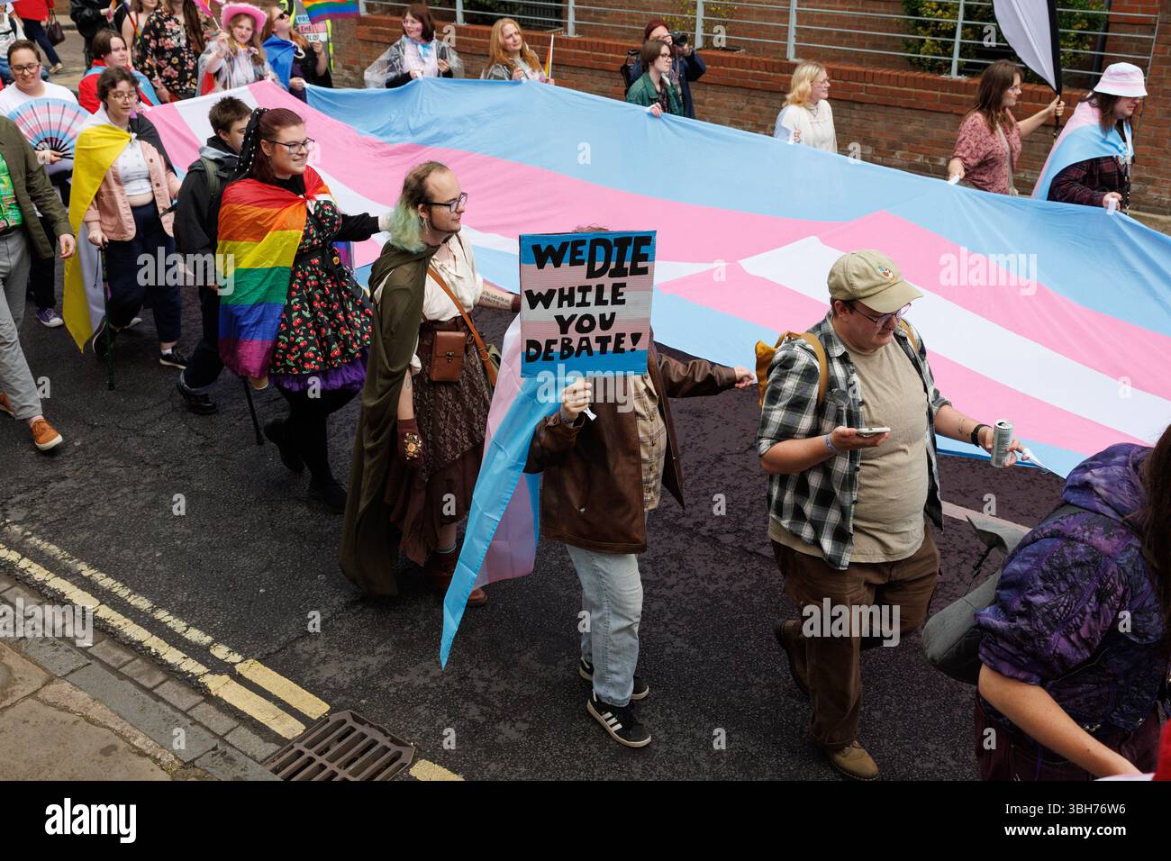 York, Großbritannien. 7. Juni 2025. Transgender- und Nichtbinäre marschieren während der Parade im York Pride 2025 mit einer großen Transgender-Flagge zur Unterstützung der Transgender-Rechte. Ein Mitglied der Fraktion hält ein Plakat mit dem Aufdruck "Wir sterben, während Sie debattieren" hoch. Quelle: Katy Blackwood/Alamy Live News Stockfoto