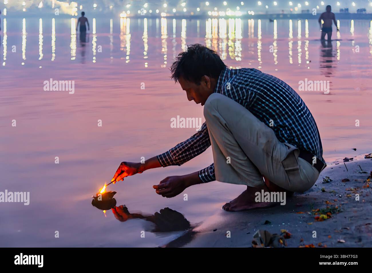 Prayagraj, Indien - 26. Februar 2025: Mann hockt am Fluss während Kumbh Mela in Indien und zündet eine schwimmende Lampe in einem heiligen Ritual an. Stockfoto