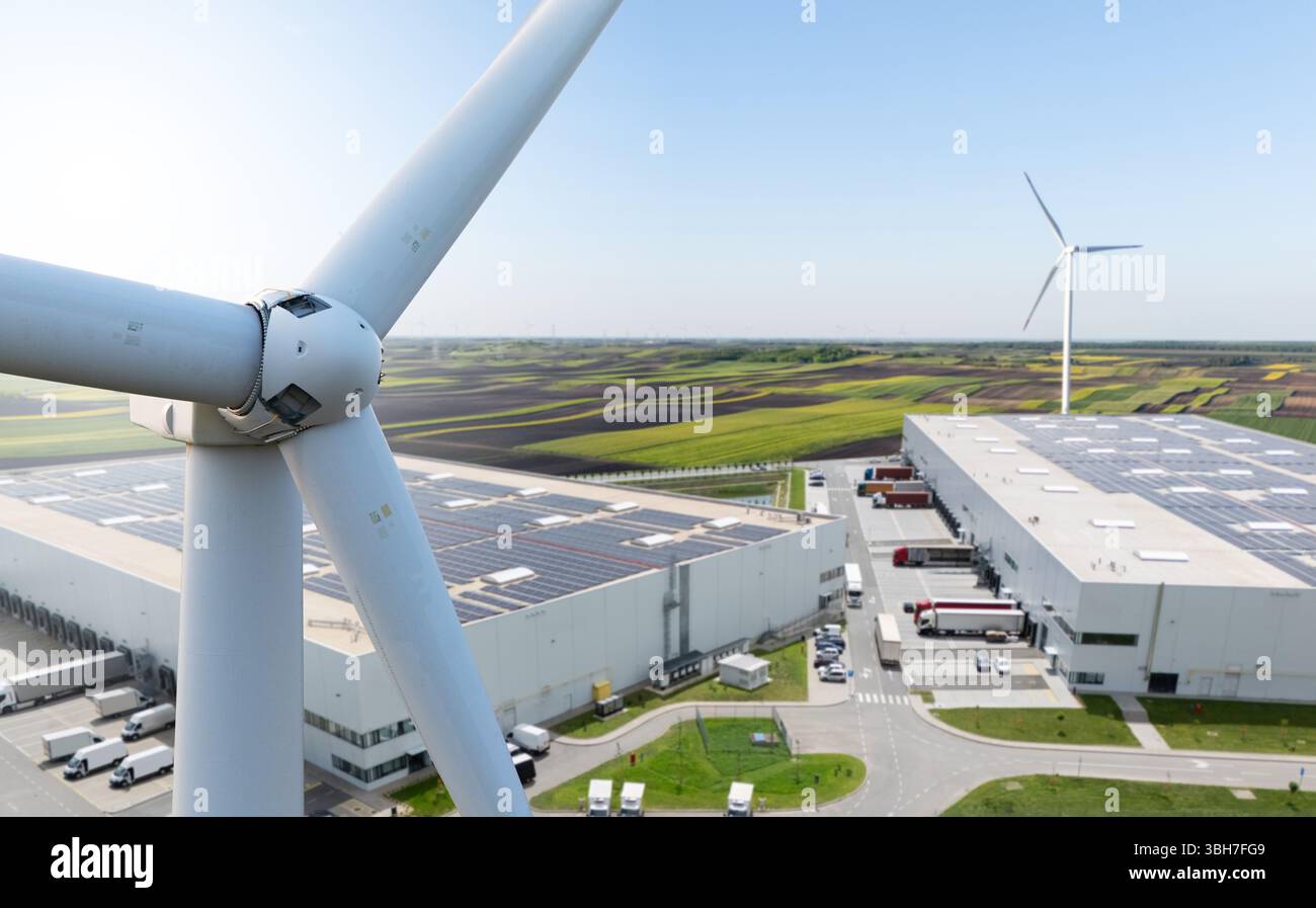 Windkraftanlage auf einem Hintergrund von Logistikzentren mit Solarpaneelen auf Dächern. Stockfoto