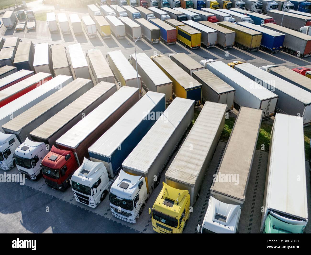 Aus der Vogelperspektive eines großen LKW-Parkplatzes an einem Logistikzentrum mit mehreren gewerblichen Sattelzügen, die in organisierten Reihen geparkt sind. Blickwinkel der Drohne Stockfoto