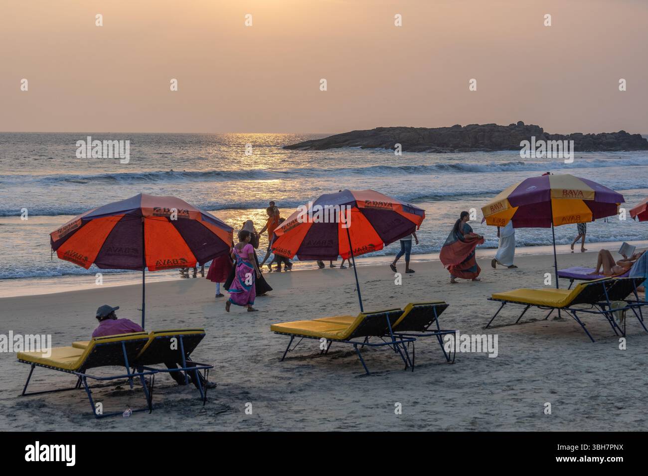 Leute gehen und entspannen bei Sonnenuntergang unter Sonnenschirmen am Kovalam Beach, Kerala, Südindien Stockfoto