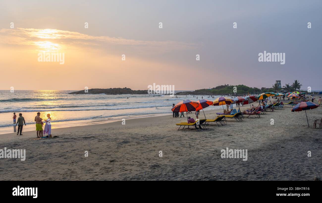 Kovalam Beach bei Sonnenuntergang mit farbenfrohen Sonnenschirmen und Menschen, die sich auf dem Sand entspannen, Kerala, Indien Stockfoto
