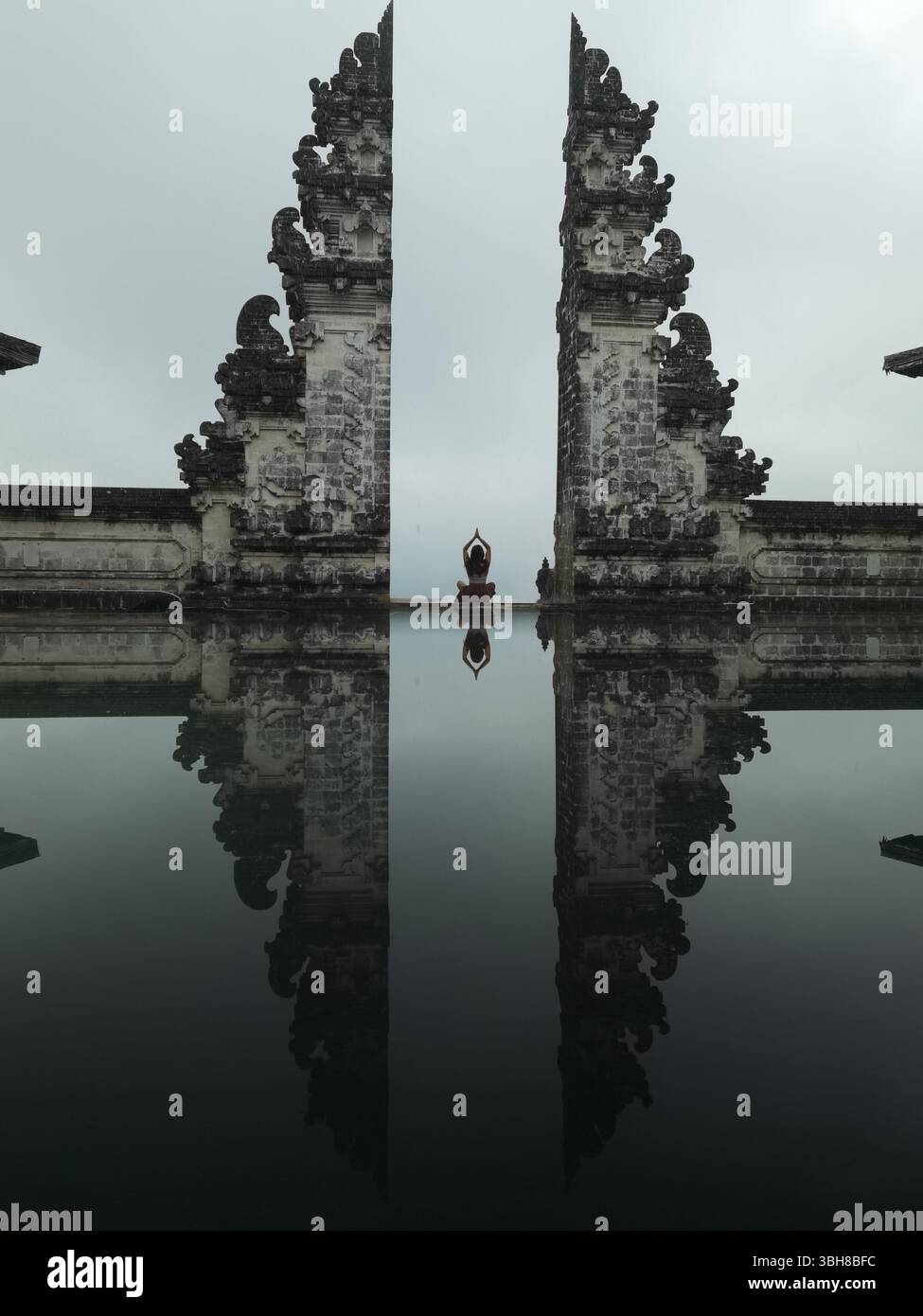 Frau meditiert, Tempeltore, Lagunenspiegelung. Eine Frau meditiert ruhig zwischen den ikonischen Toren des Lempuyang Tempels in Bali, ihre Silhouette mir Stockfoto