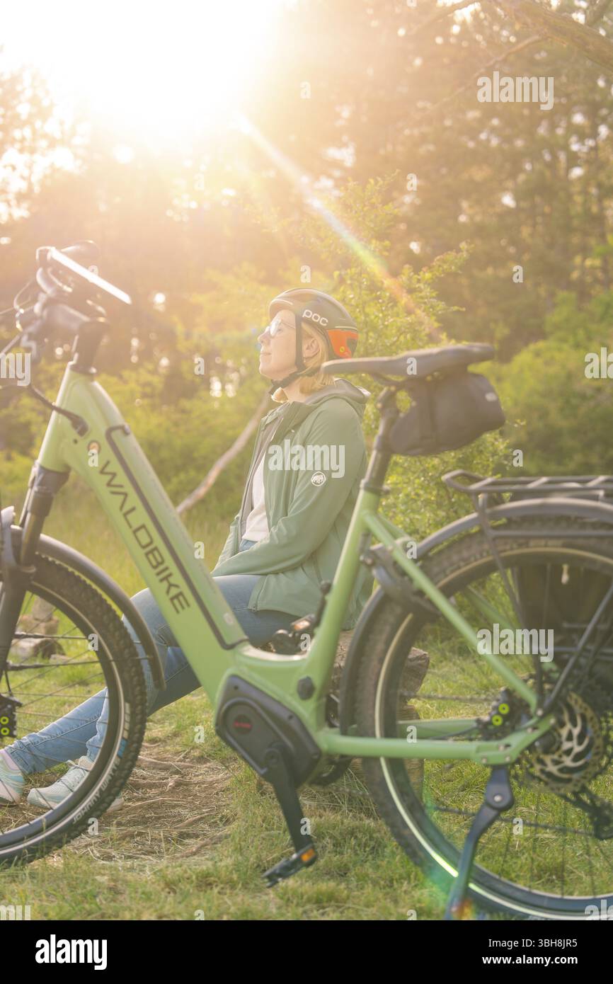 Person mit Helm, die neben einem Fahrrad sitzt, die Natur im warmen Sonnenlicht genießen, E-Bike-Ausflug, Gechingen, Landkreis Calw, Deutschland, Europa Stockfoto