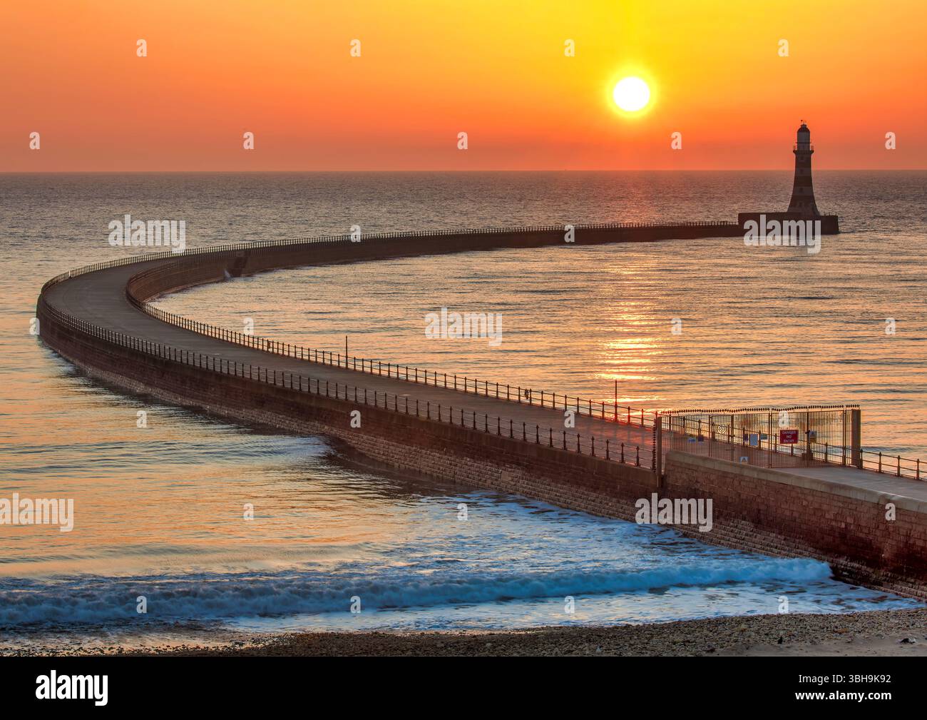Ein Blick bei Sonnenaufgang im Herbst mit Sonnenaufgang über dem Roker Pier und dem Leuchtturm in Sunderland in einen klaren Himmel, der die gesamte Kurve des Piers zeigt Stockfoto