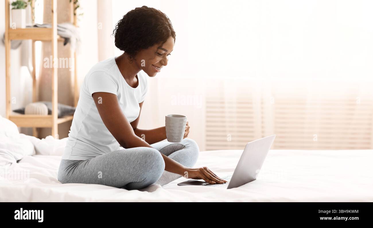 Glückliche Frau mit einer Tasse Tee mit Laptop im Bett Stockfoto