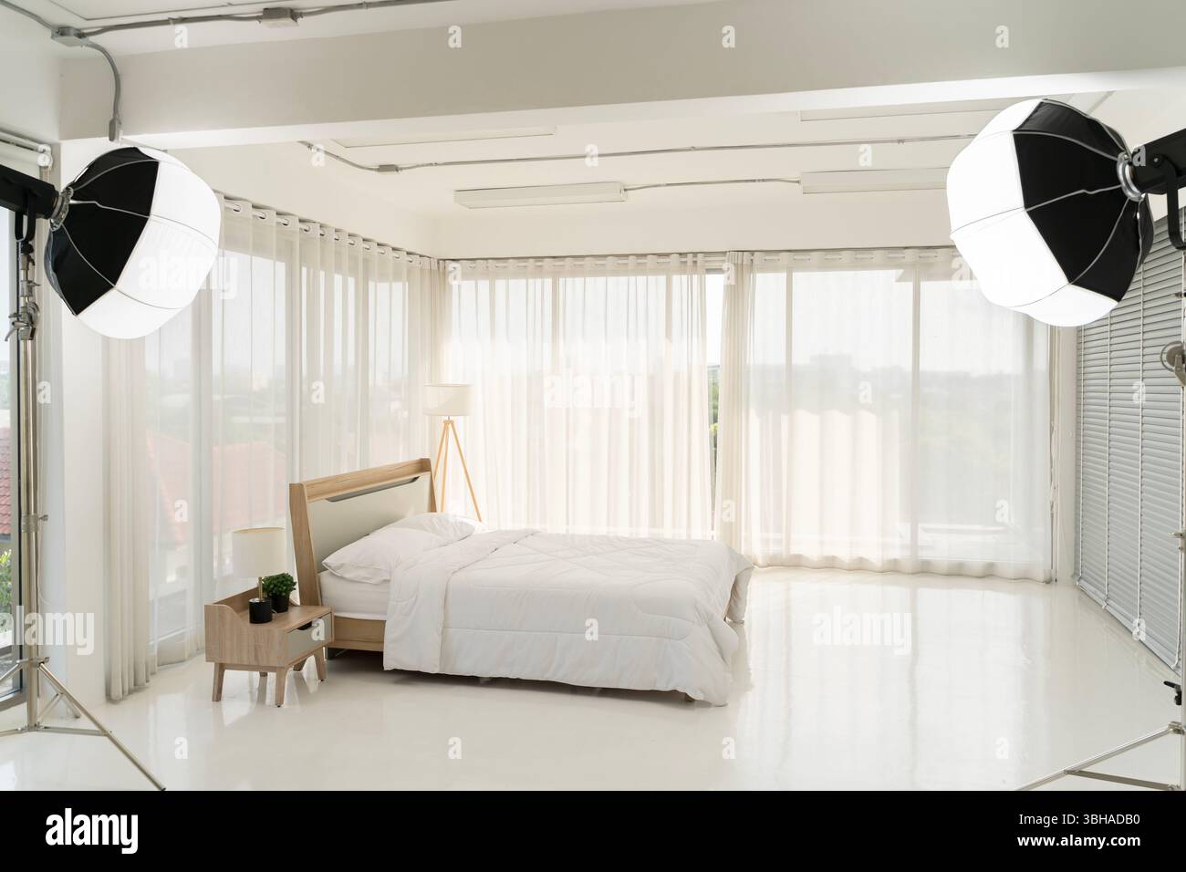 Modernes Schlafzimmer mit Tageslicht, weißen Vorhängen, Bett und minimalistischer Einrichtung. Studio-Leuchten für Innenaufnahmen, Heimdesign-Shooting oder Rea Stockfoto