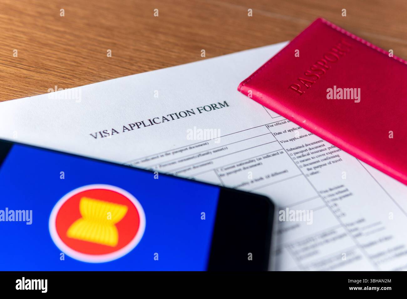 Einen Reisepass, ein Visumantragsformular und ein Smartphone mit der ASEAN-Flagge auf einem Holztisch. Internationales Reisekonzept und globales Verbindungskonzept Stockfoto