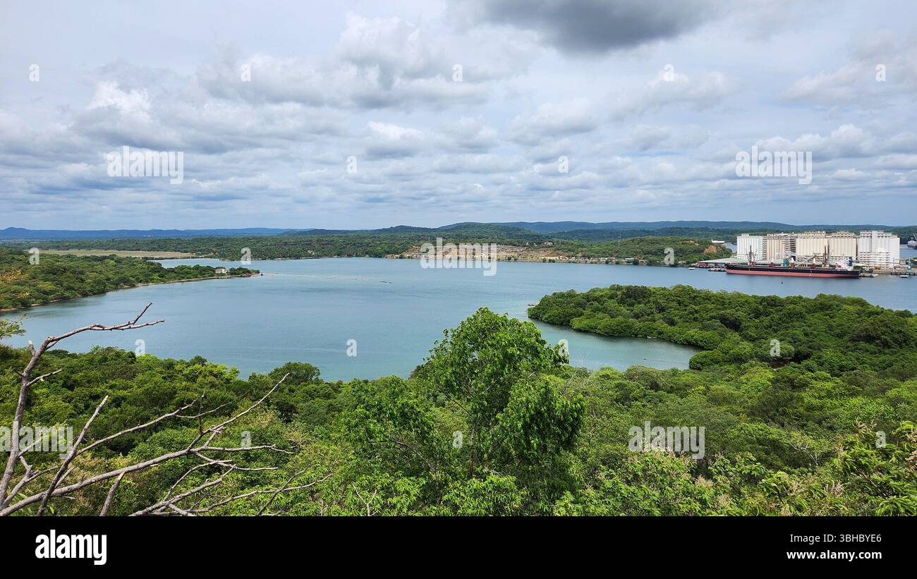 Malerischer Blick auf eine Küstenlagune mit üppigen grünen Mangroven, klarem blauem Wasser und einem Industriehafen in der Ferne unter einem bewölkten Himmel, sri lanka. - Smartphone-aufgenommenes Stockfoto