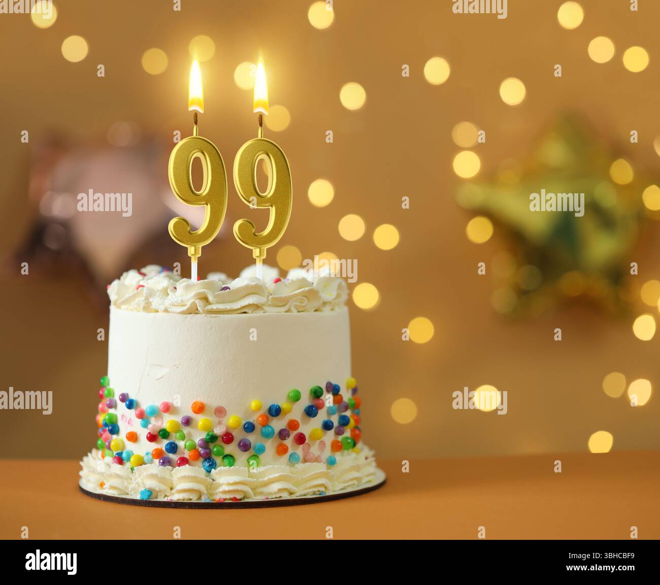 Leckerer Kuchen mit brennenden, nummerförmigen Kerzen vor verschwommenem Licht, Platz für Text. 99. Geburtstag oder ein anderer besonderer Anlass Stockfoto