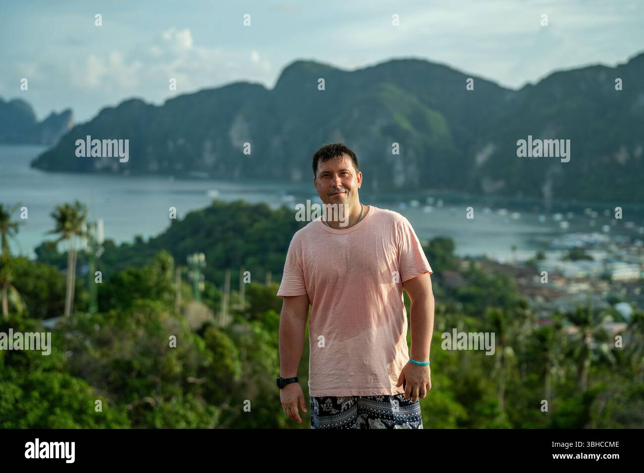 Ein Mann in einem rosa nassen T-Shirt steht vor der Kulisse der Insel Pi Pi Don Stockfoto