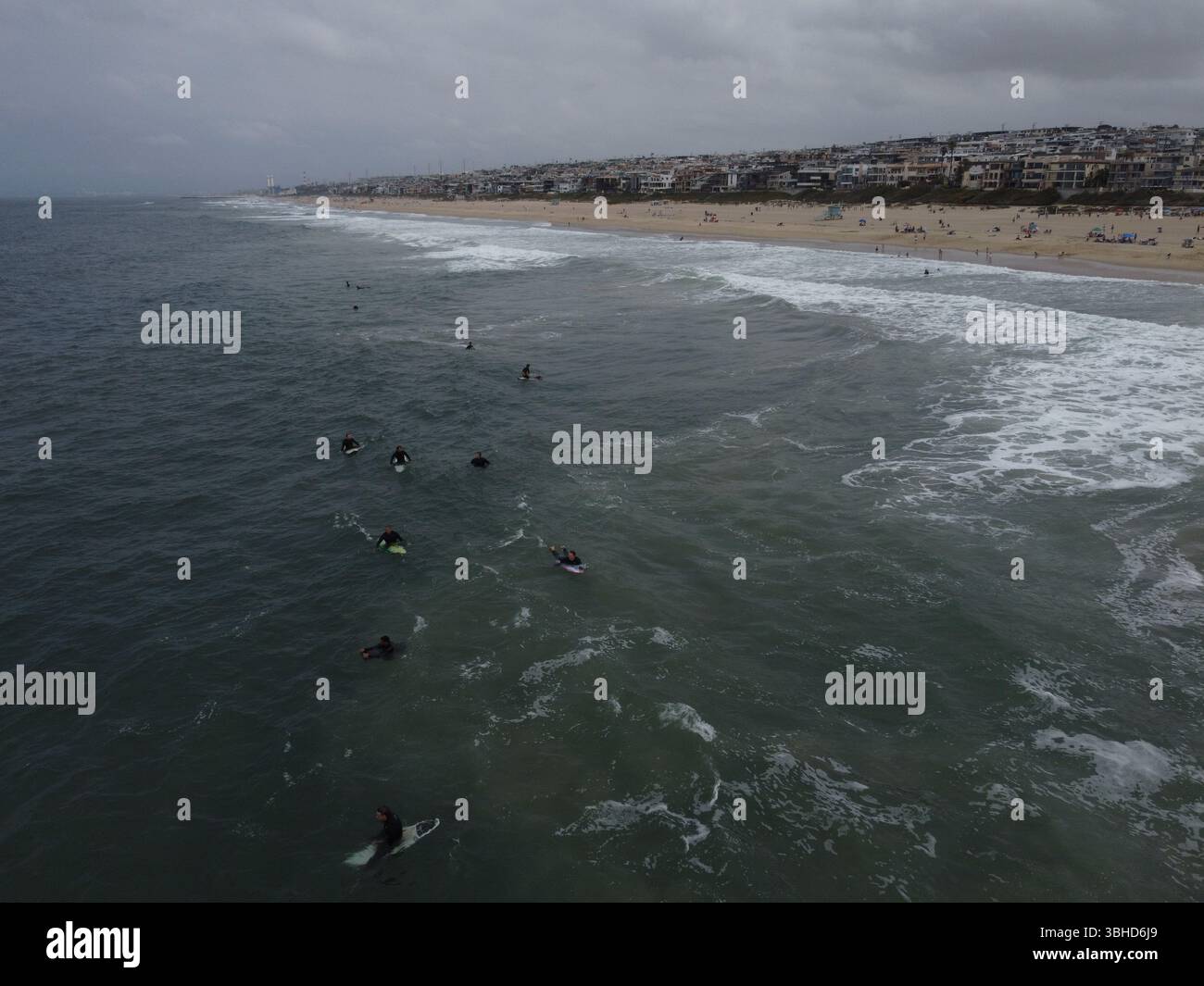 Aus der Vogelperspektive sehen Surfer, die in der Nähe des Manhattan Beach Pier unter stimmungsvollem Himmel Wellen fangen – Kaliforniens Küste in Bewegung von oben. Stockfoto