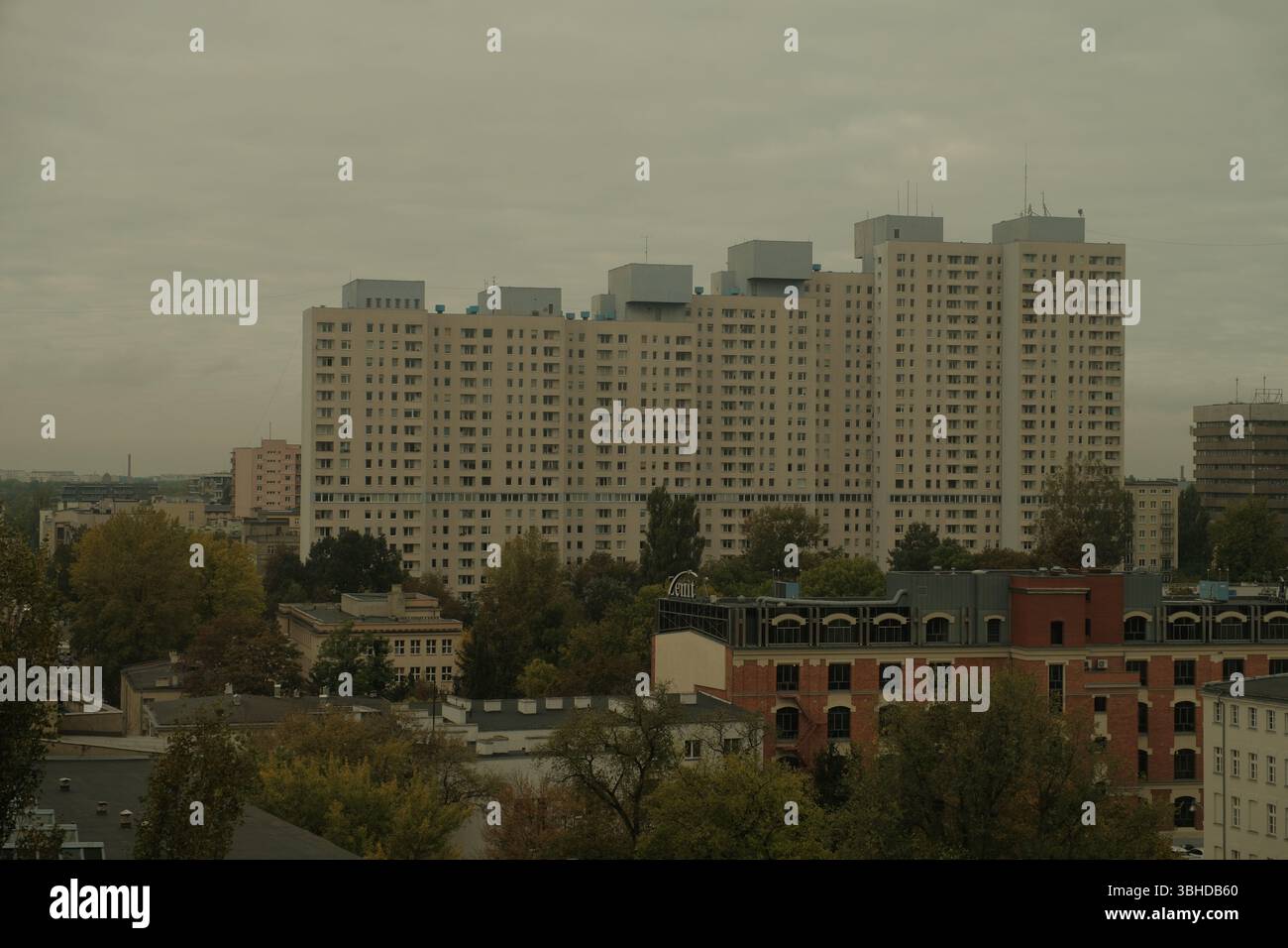 Bedeckte Stadtlandschaft von Łódź, Polen, mit einem dominanten Blick auf einen großen, ikonischen Wohnblock aus der kommunistischen Ära, der über älteren Backsteingebäuden thront. Stockfoto