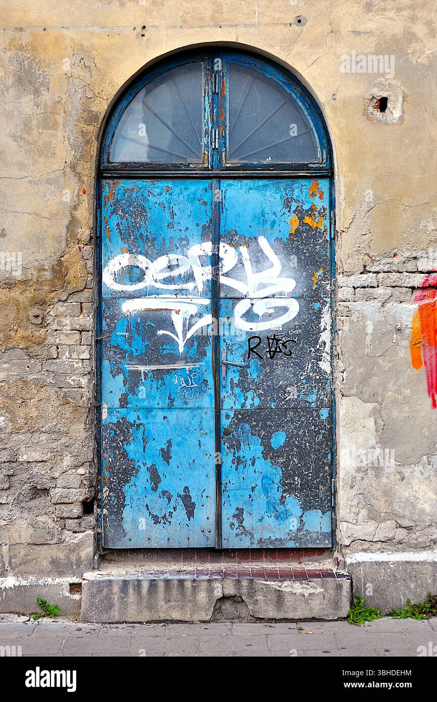 Alte blaue Tür mit Graffiti an der verwitterten Wand des verlassenen Gebäudes Stockfoto