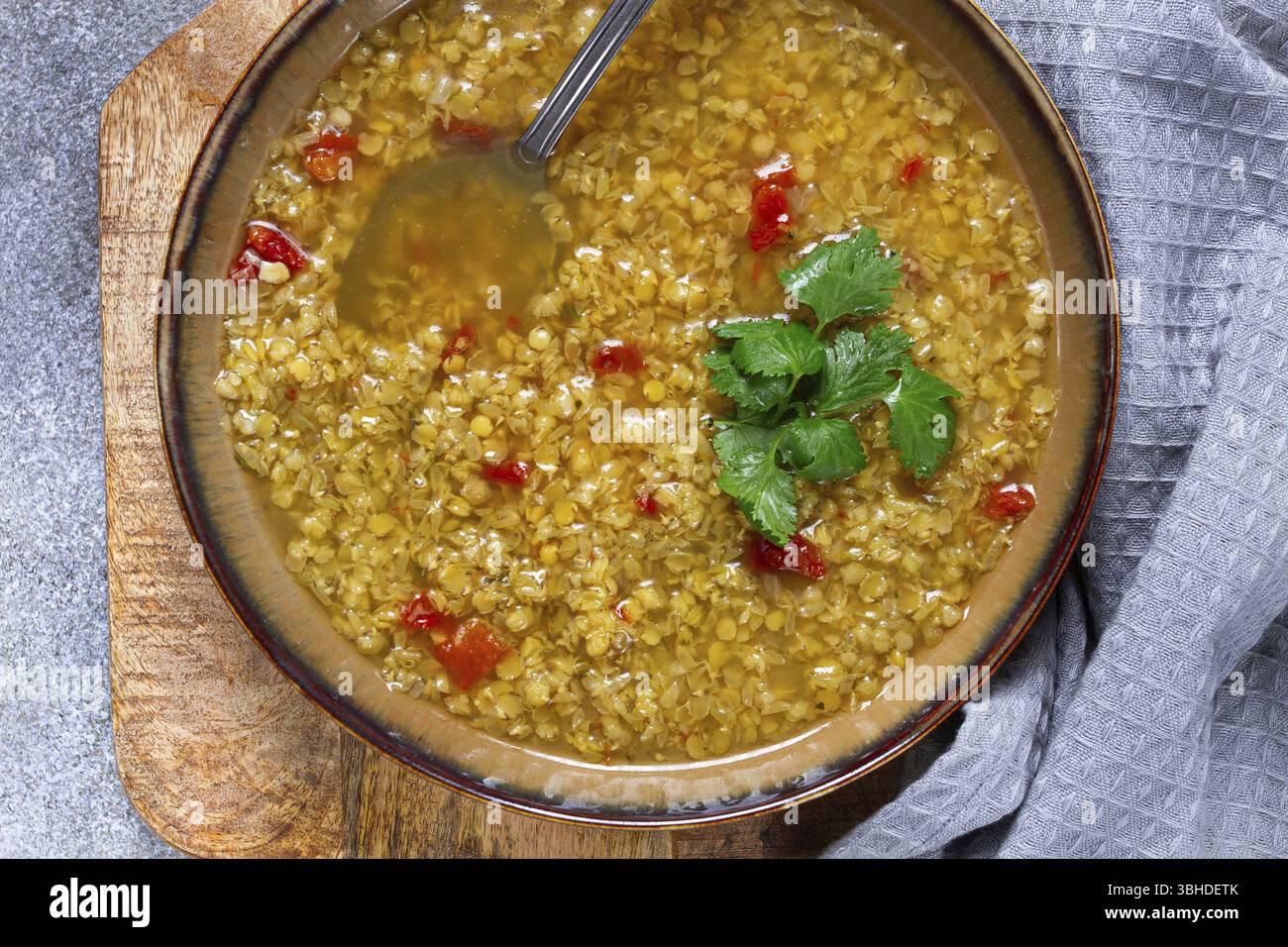 Eine herzhafte Schüssel Linsensuppe garniert mit frischen Kräutern sitzt auf einem Holzbrett. Die warmen Farben und Texturen sorgen für ein angenehmes Speiseerlebnis Stockfoto