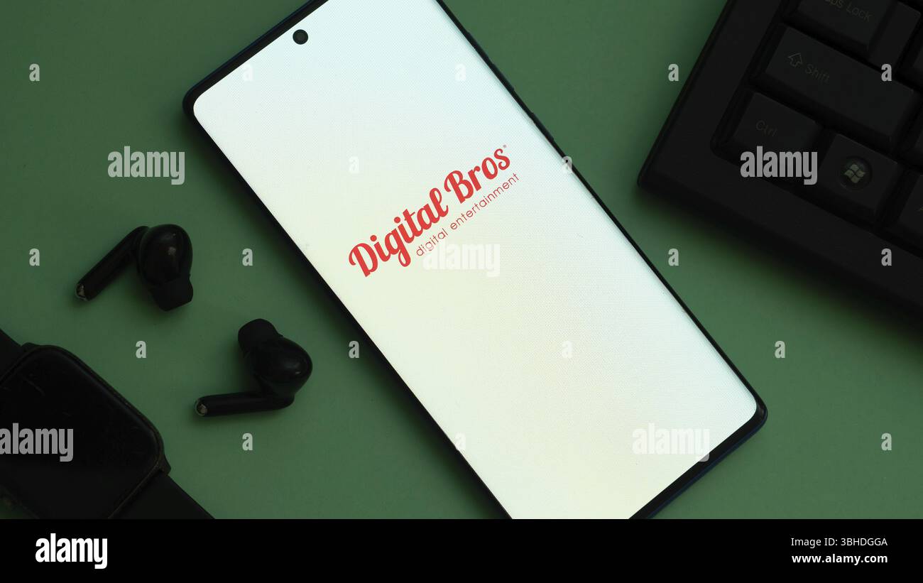 Smartphone mit Digital Bros Logo neben Ohrhörern und Smartwatch auf grünem Hintergrund Stockfoto