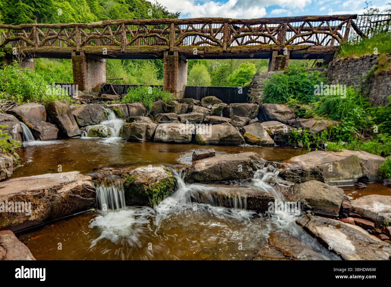 Die rustikale Oak Bridge im National Botanic Garden of Wales, Carmarthenshire, Wales, mit rauschendem Fluss Towi über Felsen im Vordergrund. Verlockend Stockfoto