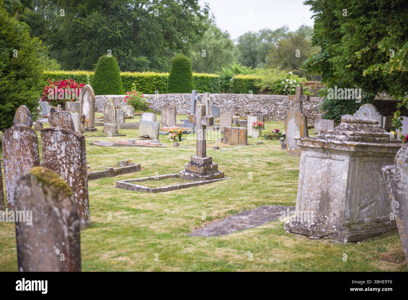 Alter englischer Friedhof mit verwitterten Grabsteinen bedeckt mit Moos und Flechten. Friedlicher ländlicher Friedhof, Großbritannien. Keine identifizierbaren Grabsteine. Stockfoto