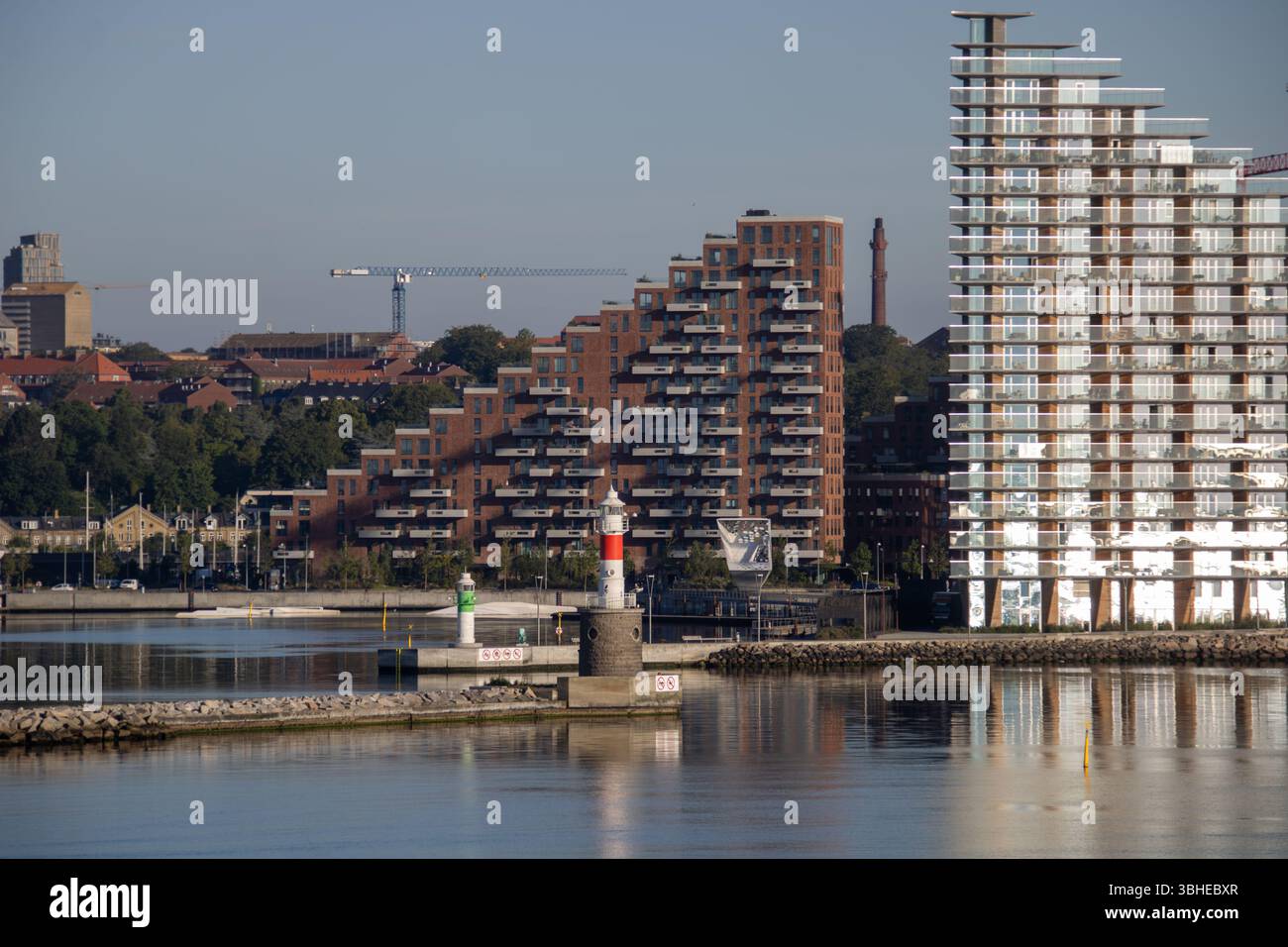 Aarhus, Dänemark: Leuchtturm „Bugten Fyr“ vor Skyline von Aarhus Ø mit Wohnkomplex „Isbjerget“ und Hochhaus „Light*House“ am Wasser Stockfoto
