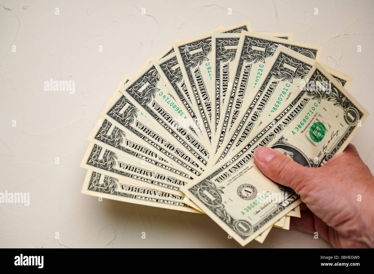 Hand mit verschiedenen Stückelungen von US-Währung angeordnet, aufgefächert vor einem hellen Hintergrund Stockfoto