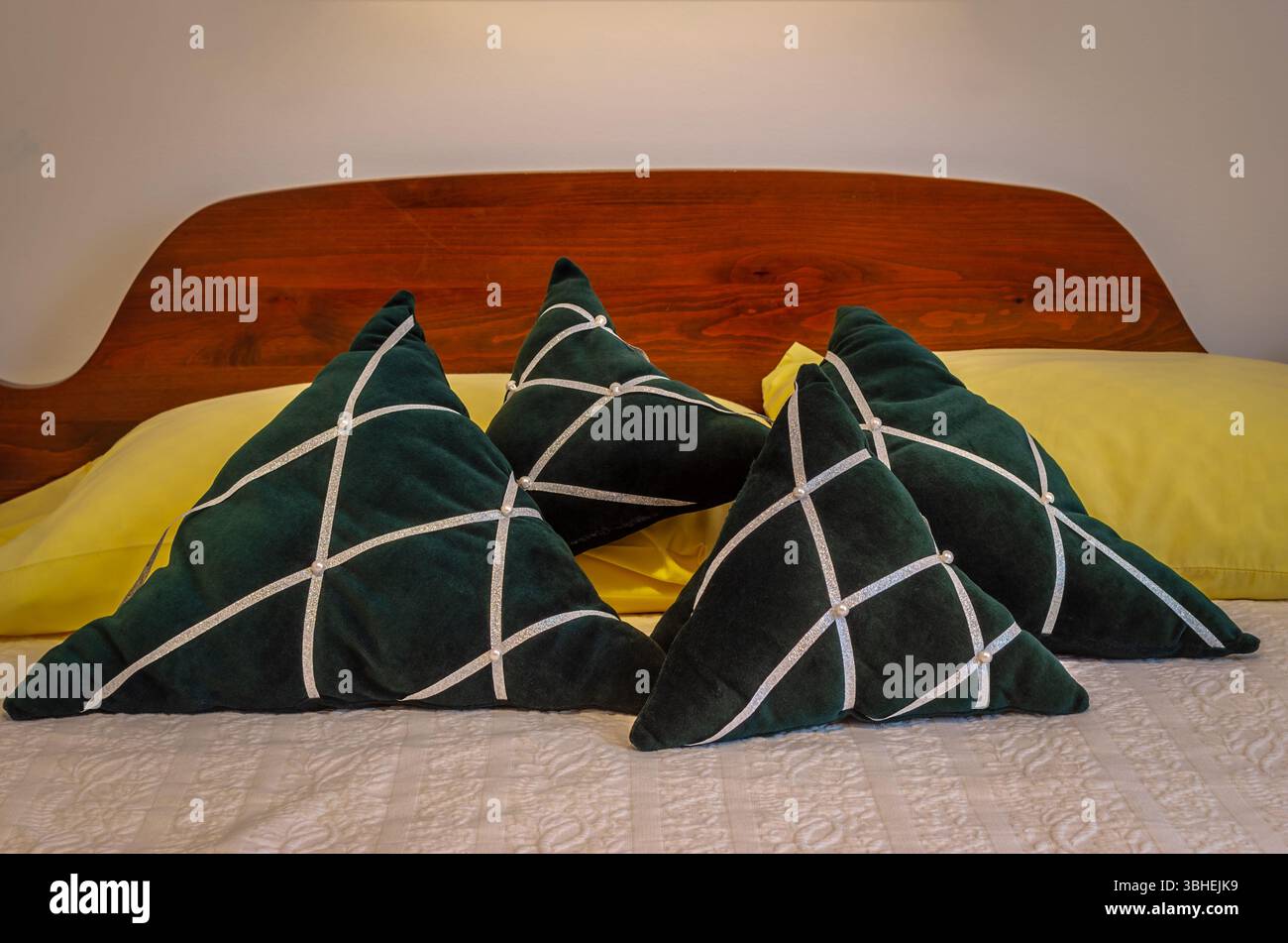 Vier grüne Samtkissen mit Weihnachtsmotiv auf einem Bett mit einem Kopfteil aus Kiefernholz. Stockfoto