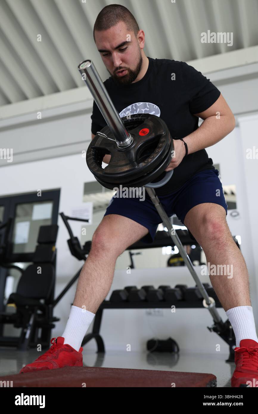 Ein Mann hebt in einem Fitnessstudio eine Hantel mit Gewichten an und zeigt damit die Hingabe zum Krafttraining. Er konzentriert sich intensiv auf sein Workout im Fitness-Equ Stockfoto