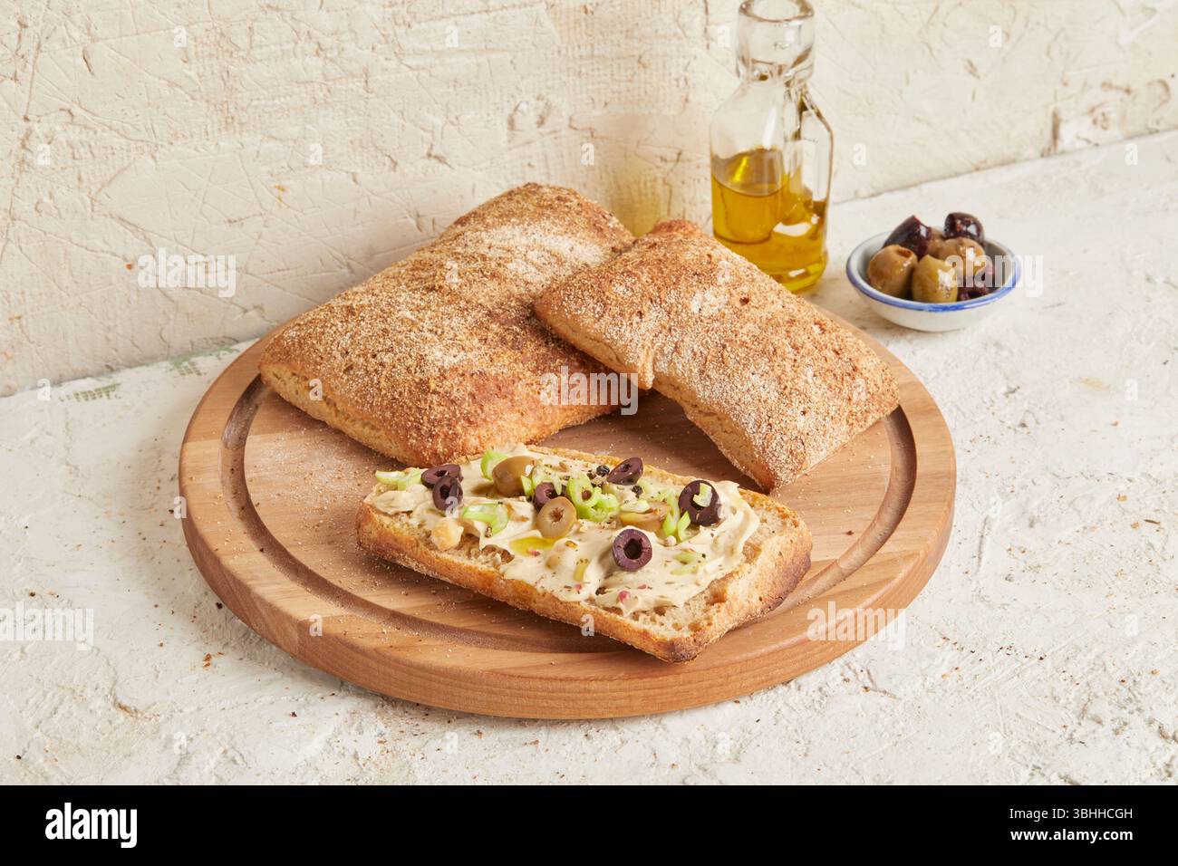 Dinkel-Ciabatta auf Holzoberfläche mit Oliven und Olivenöl im Hintergrund – ein rustikales Brot im mediterranen Stil, perfekt für Aperitif. Stockfoto