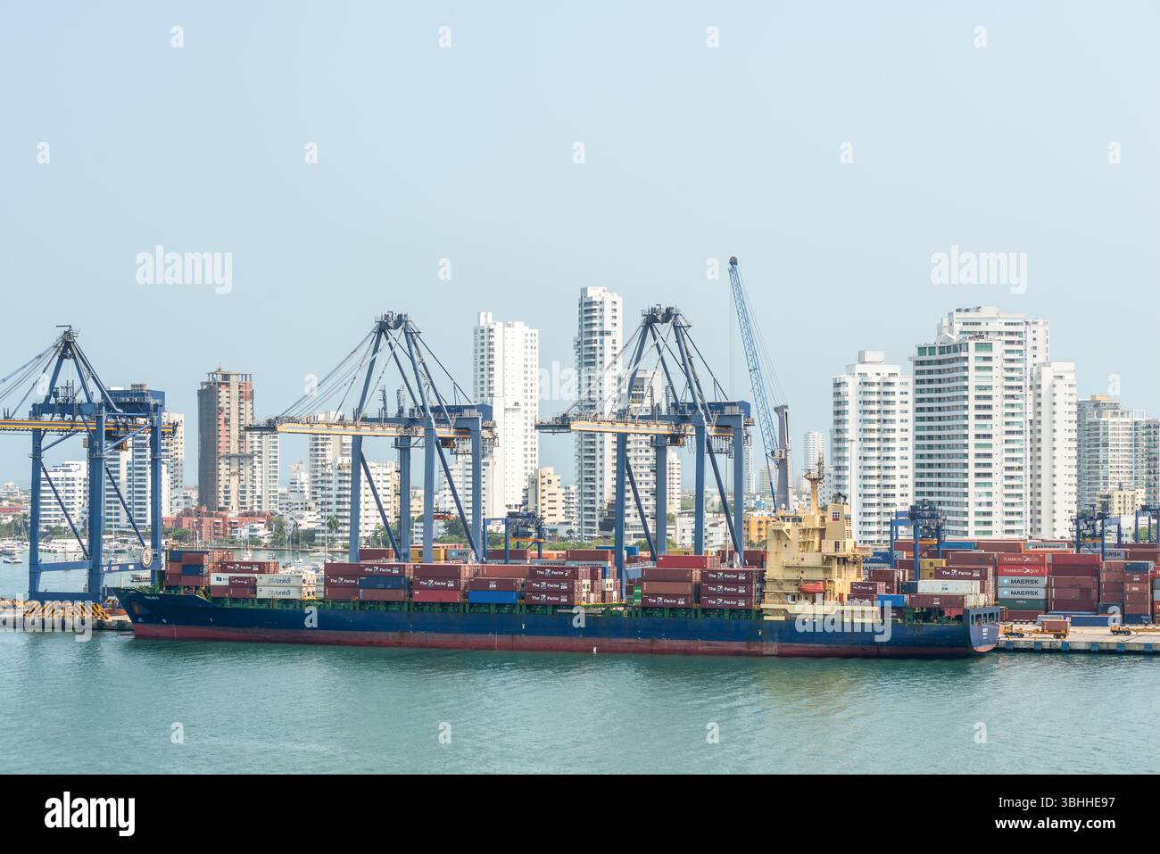 Cartagena, Kolumbien - 12. April 2024: Die Hafenszene zeigt das Containerschiff Chloe D, Kräne und Schiffscontainer mit den hohen Gebäuden von Cartagena Stockfoto