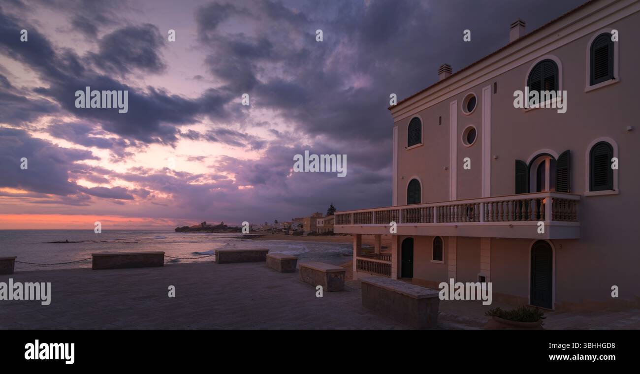 Die goldene Dämmerung strahlt einen magischen Glanz über Punta Secca aus und hebt die ruhige Küste und die bezaubernde Architektur Siziliens hervor Stockfoto