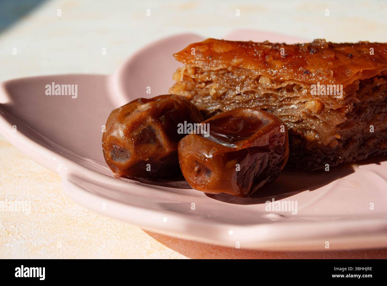 Köstliches Baklava-Dessert und süße Datteln wunderschön auf einem dekorativen rosafarbenen Teller angeordnet. Stockfoto