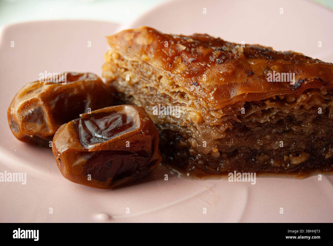 Köstliches Baklava-Dessert und süße Datteln wunderschön auf einem dekorativen rosafarbenen Teller angeordnet. Stockfoto