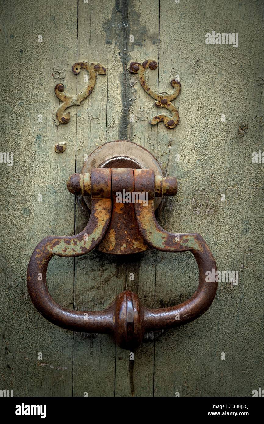 Ein alter, rostiger Türklopfer liegt auf einer verwitterten Holztür und zeigt komplizierte Designs und die Auswirkungen der Zeit. Stockfoto