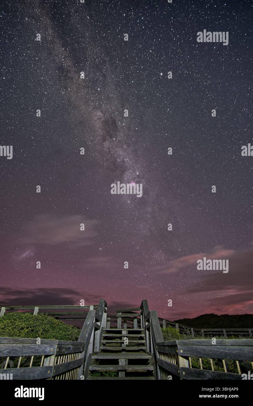 Blick auf eine Treppe in den Nachthimmel mit Milchstraße und leichter aurora über die Küste und das Meer in Point Addis, Victoria, Australien Stockfoto