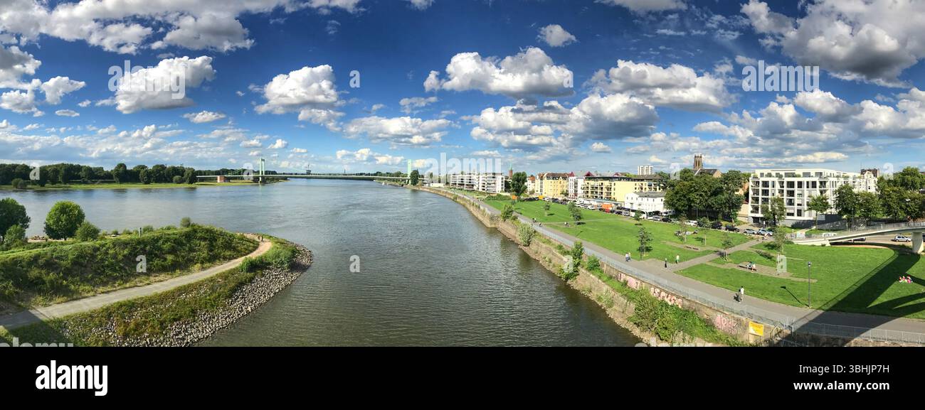 Weites Panorama auf einen ruhigen Fluss mit üppigem Grün, malerischer urbaner Landschaft und ruhigem Wasser. Stockfoto