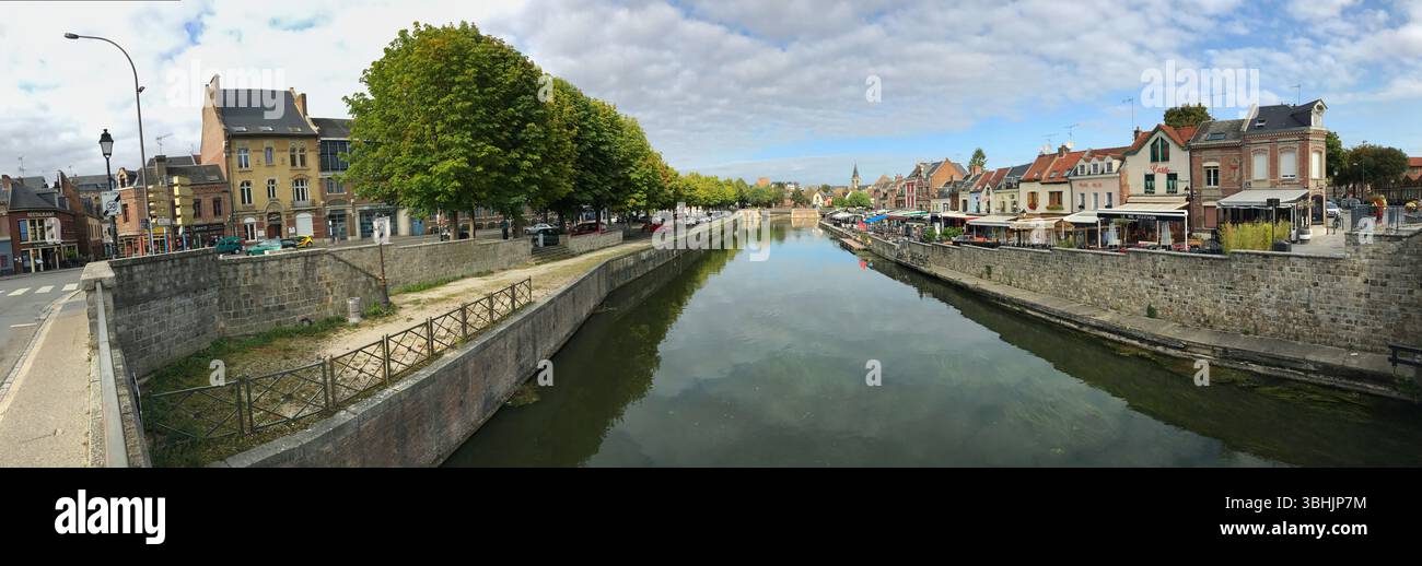 Ein breiter Panoramablick auf einen ruhigen Fluss, gesäumt von historischen Häusern und Grün, bietet eine ruhige und malerische Atmosphäre in einer malerischen Umgebung Stockfoto